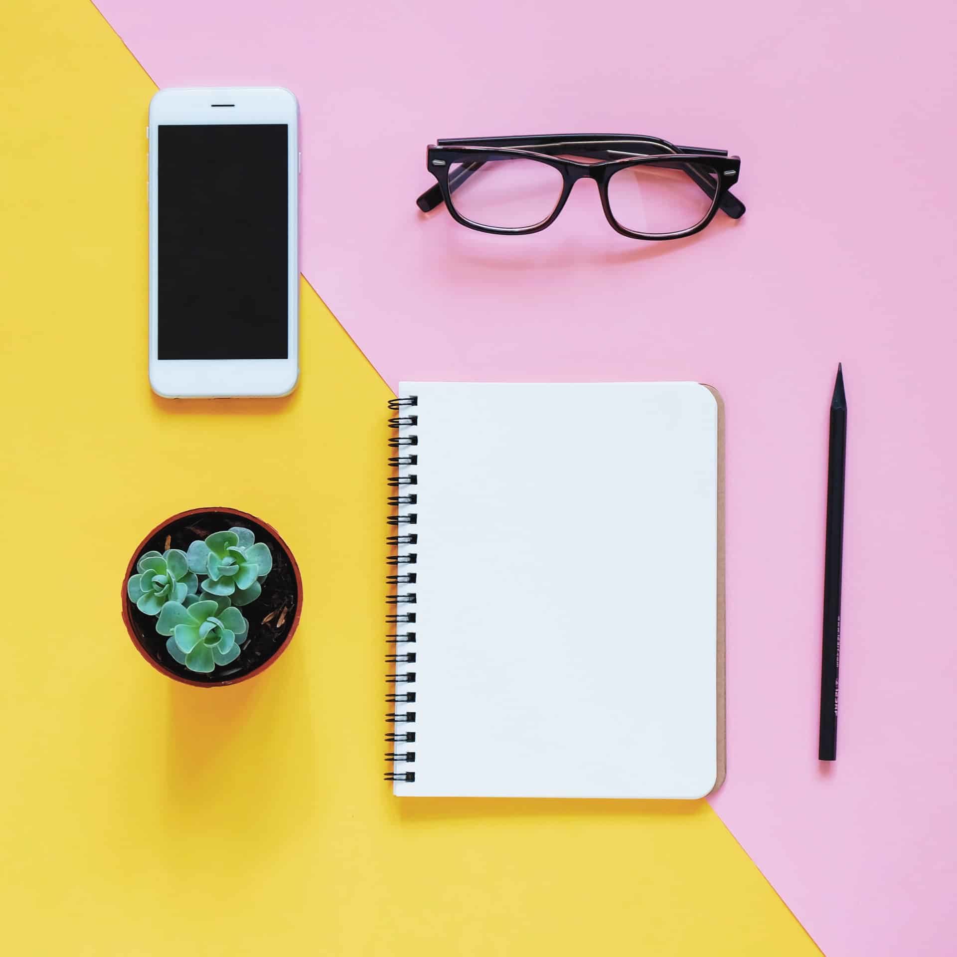 Creative flat lay photo of workspace desk with smartphone, eyeglasses, cactus and notebook with copy space background, minimal style